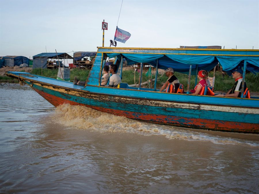 Colorful local motorboat carrying passengers past riverside homes in rural Cambodia