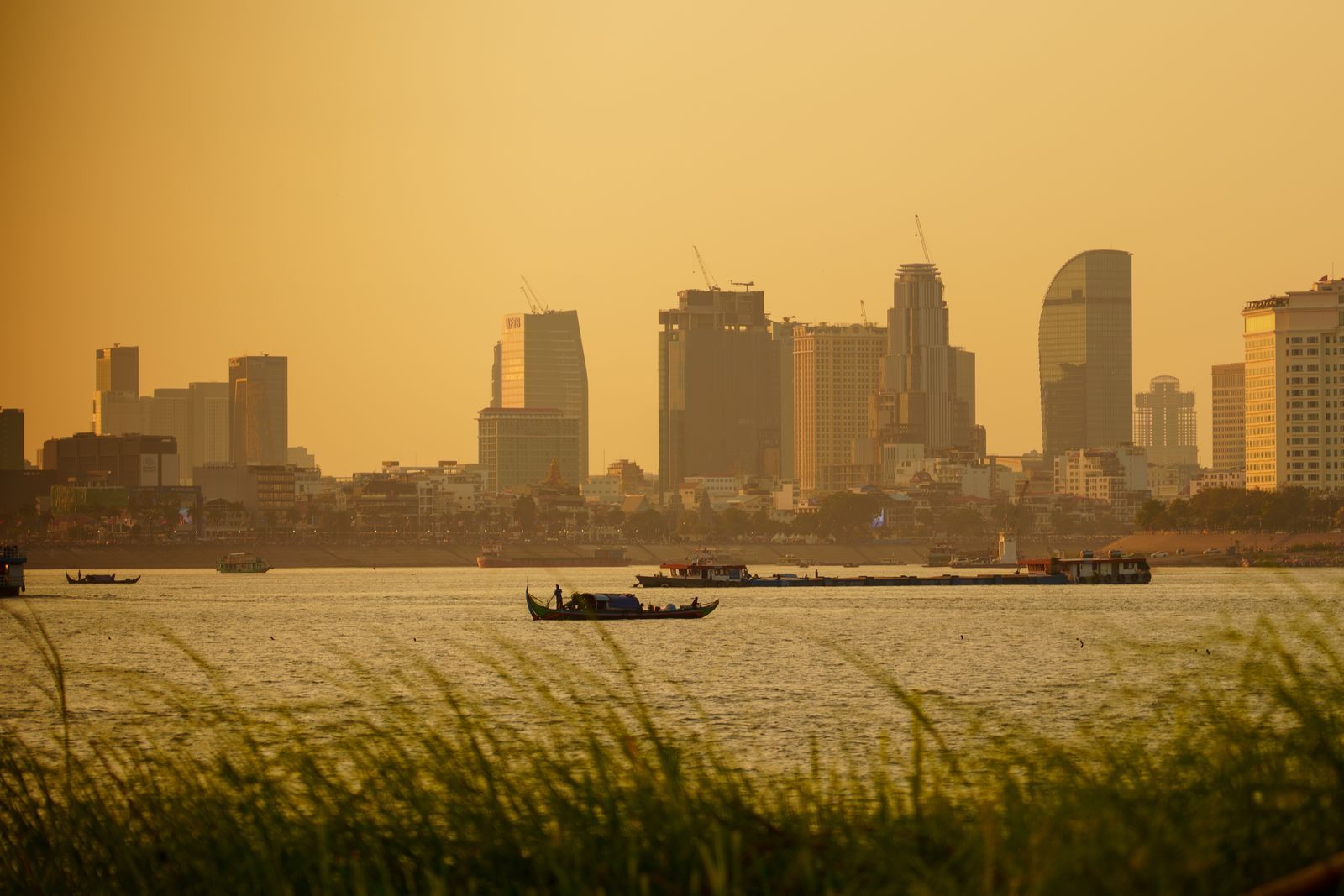 Hazy golden sunset over the river at Phnom Penh with a small boat crossing below the skyline, the view from a Cambodia river cruise